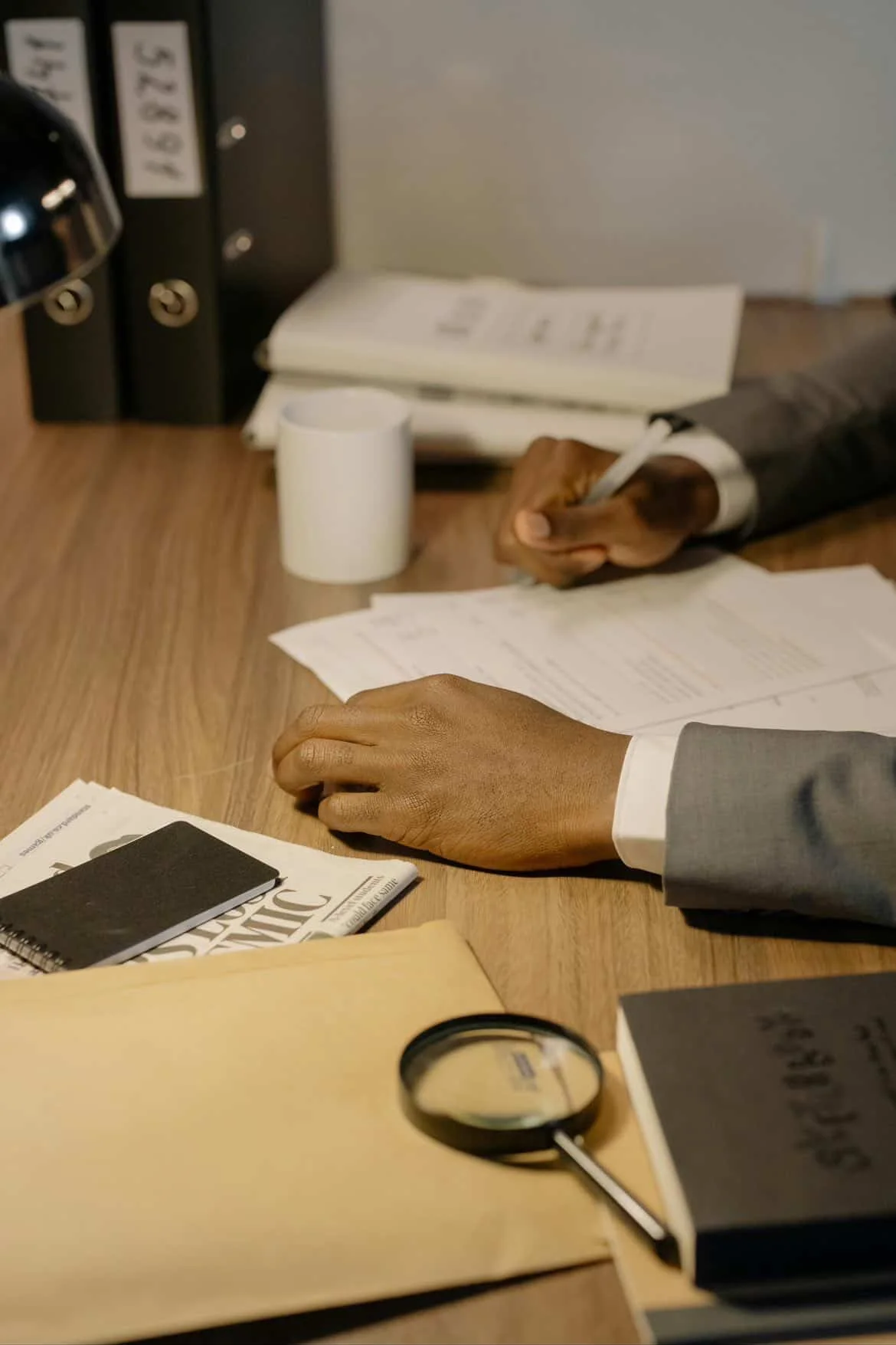 Private investigator reviewing documents and writing case notes at an office desk